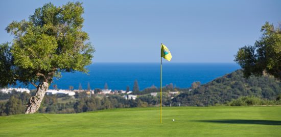 Campo de golf en Estepona con bandera amarilla, calles verdes y el mar Mediterráneo al fondo.