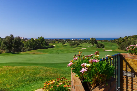 Campo de golf en Marbella con exuberantes calles verdes, flores en primer plano y el mar Mediterráneo al fondo.