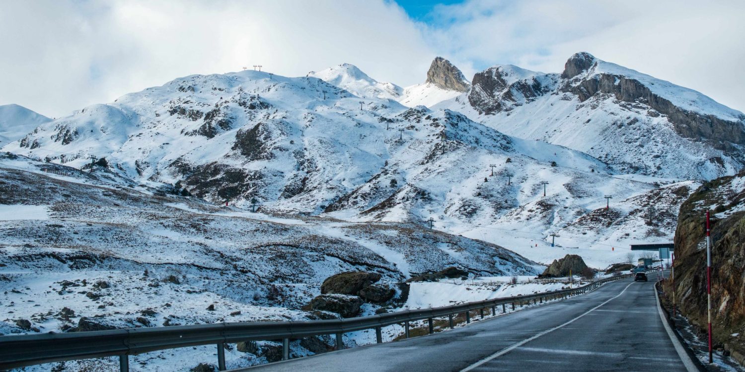 Carretera nevada rodeada de altas montañas rocosas bajo un cielo nublado