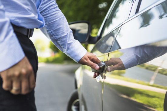 A man in a blue shirt unlocking a rental car door.